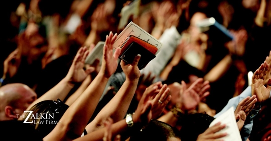 Crowd of people raising their hands holding bibles.